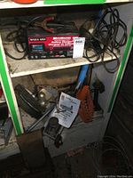 Overall shelf view showing battery charger, floor jack, traction pads, rear hitch, and trouble light with cables.