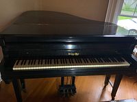 Front view of the black Kranich and Bach baby grand piano showing keyboard and name branding