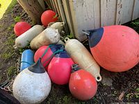 All 12 buoys in a cluster on ground near wooden wall with visible weathering and dirt
