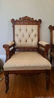 Front view of a vintage Eastlake carved wooden chair with peach and gold patterned upholstery, tufted backrest, and casters.