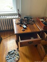 End table with drawer open showing some wear, scratches, and drawer hardware. Various decorative items on table surface not included.
