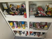 Wide shot of shelves showing various cleaning sprays, adhesives, tapes, small tools, and bottles arranged in cubby compartments.