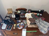 Full view of men's accessory items displayed on wooden cabinet including bow ties, handkerchiefs, pins, cuff links, lighters, shoe shine products, wallet, watch, utility tool, and wood box.