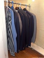 Photo of striped button down shirt, light blue sweater, and several dress jackets hung on hangers in closet.