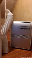 Full view of the white upright portable air conditioner and attached flexible vent hose.