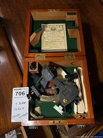 Open wooden sextant case showing black metal sextant, telescope, micrometer scale and green felt interior.