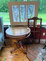 Round wooden table with a leather inlaid top, drawer open showing interior, set beside window frames and metal pot holder.