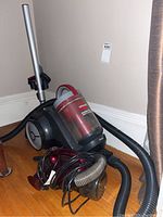 Bissell canister vacuum and small portable Shark handheld vacuum placed on a wood floor against a wall.
