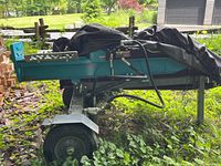 Side view of the teal-painted hydraulic log splitter on a towable frame, partially covered.