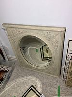 Full view of carved off-white wood framed oval mirror showing beveled glass and floral vine carvings on the frame.