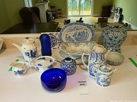 Wide shot of blue and white Royal Copenhagen tea set, including pot, creamer, sugar bowl, plates, two ceramic tiles, and cobalt blue glass pieces.