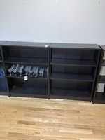 Front view of two dark wood bookshelves side by side showing three shelves each, minor wear noted, glasses on one shelf not included