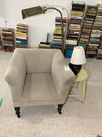 Vintage beige armchair, floor lamp, table lamp on wood stool with background stacks of books