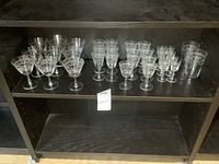 Wide view of multiple etched crystal stemmed glasses arranged on shelf showing various sizes and styles.