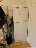 Front view of tall white cupboard against wall next to door, showing 4 door handles on two sections.
