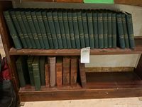 Shelf with 25 green cloth hardcover Dickens Works volumes marked with gold text on spine, showing minor wear.