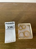 Photo showing three pairs of earrings in a box on a wooden surface with a MaxSold auction card.