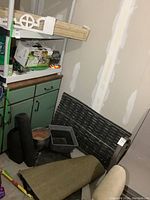 Wide view showing black rubber mats rolled and flat, wooden planter box standing on edge, plastic planter pots and gardening gloves on floor by green cabinet