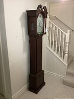 Full view of wooden grandfather clock case beside staircase