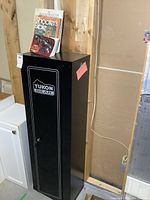 Full view of black Yukon Gear metal cabinet showing tall narrow structure next to a white cabinet and books placed on top