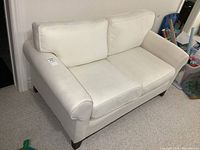 Front angled view of off white fabric loveseat with two cushions, showing arm and seat.