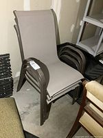 Set of three stackable outdoor patio deck chairs with brown metal frames and beige mesh seats and backs, shown stacked against a wall in a garage or storage area.