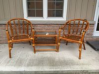 Full view of bamboo patio furniture set including two chairs and table on concrete step in front of brick wall.