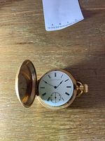 Full hunter case open to reveal white enamel dial with black Roman numerals, subsidiary seconds at 6, and blued steel spade hands