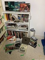 Shelf with railroad books, VHS tapes stacked on floor, cards and other printed material arranged around shelf.