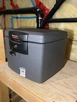 Front and slightly angled view of gray Sentry fire safe with black lock panel and keys inserted on wooden surface in unfinished basement.