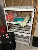 White resin 4-tier plastic shelving unit with vented slatted shelves, placed in basement with some folded items on shelf (items not included).