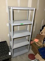 Full view of the tall plastic shelving unit with five shelves in light gray color, standing in a storage or garage space.