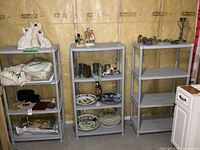 Photo showing three resin shelving units filled with various household items for display purposes. Units are gray with four shelves each, placed against unfinished basement wall.