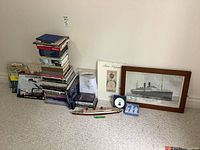 Wide shot of the lot on carpet showing items stacked together including the framed print, books, model ship, and smaller memorabilia items.