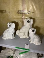 Three white porcelain Staffordshire dog figurines of varying heights displayed together on a gray surface.