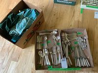 Two cardboard trays and a box of storage bags on floor showing mixed flatware pieces