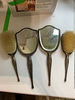 Overview of two hand mirrors and two hair brushes laid out together