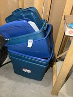 Six stacked blue Rubbermaid Roughneck storage totes, most with lids included, located in a basement.