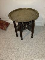 Full view of the vintage Indian folding table showing carved wood base and brass tabletop.