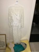 Full view of the white lace wedding dress hanging on a hanger with long sleeves and V-neckline.