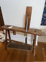 Full view of antique wooden bench showing the seat, legs, and vertical adjustable bar with strap and metal components.