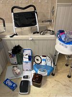 Photo showing assorted bathroom, hygiene, and medical support items arranged on floor and bathtub edge.