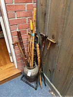Full view of the metal vase containing the collection of wooden canes and walking sticks, some with travel badges and carved designs.