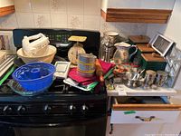 Overview of kitchen items arranged on stove and counter, showing bowls, hand mixer, scale, sifter, pitcher, canisters, utensils