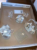 Top view of the box containing six different cut glass figurines including butterfly, mice and bear with mirrored bases