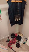 Scottish dress kilt hanging on a hanger with leather sporran attached, photo also shows black tam hat with 'Raven Clan' embroidery, white socks, red tartan sash, small bagpipe on the floor.