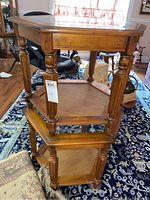 Stacked pair of hexagon wood and glass top end tables with woven lower shelves on a patterned carpet.