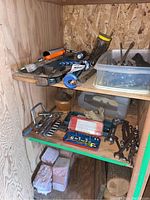 Photo shows several hand tools including socket sets, open-end wrenches, and various small items stored on wooden shelves with some bricks underneath.