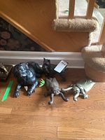 Four metal animal-shaped door stops on wooden floor near carpeted stairs: large black Labrador, black Scottie dog, two crickets (one brass, one iron).