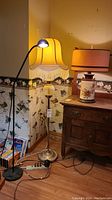 Three lamps side by side: vintage floor lamp with fringed shade and gold-tone frosted glass globe base, retro ceramic table lamp with butterfly design and paper shade, and modern black floor lamp with small lamp head.